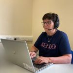 A woman typing on a laptop and wearing a head set