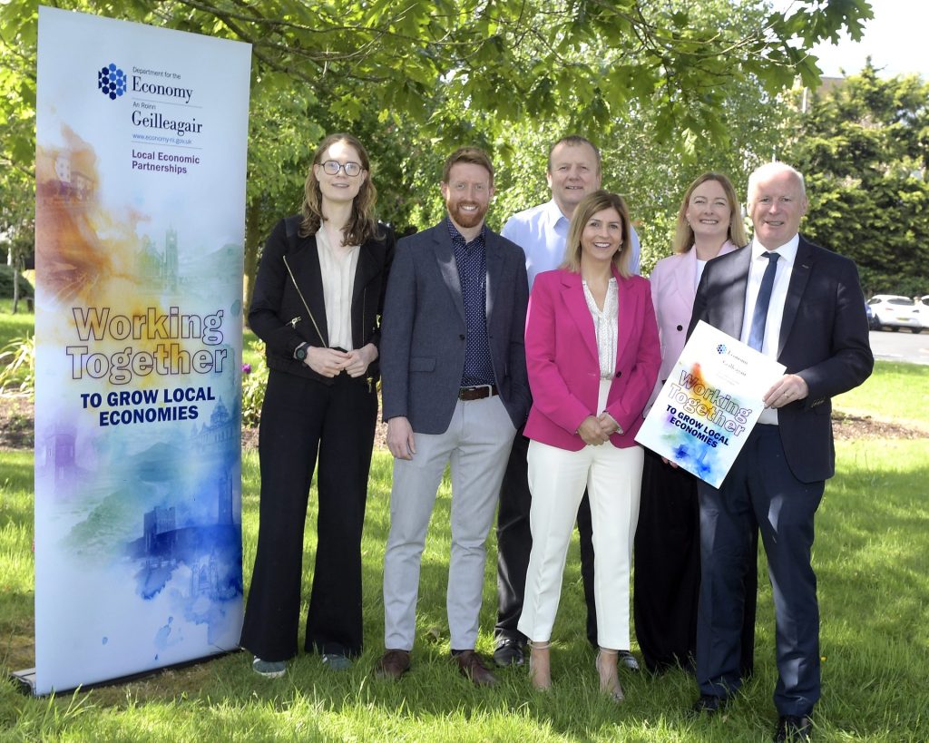 Group of people standing in a wooded area beside a Department for Economy banner.