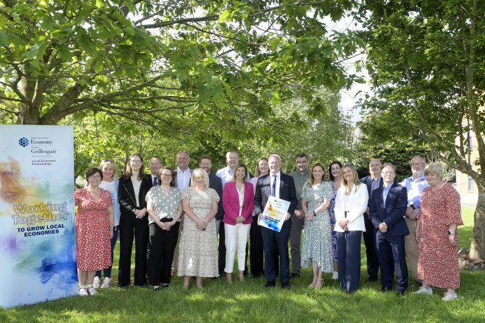 Large group of people standing in a wooded area with a Department for Economy banner.