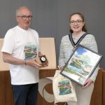 Deputy Lord Mayor holding some paintings and standing beside a male.