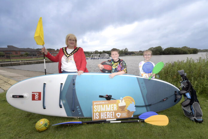 NEWS the lord mayor and 2 children standing beside a lake with a paddleboard and sports raquets.