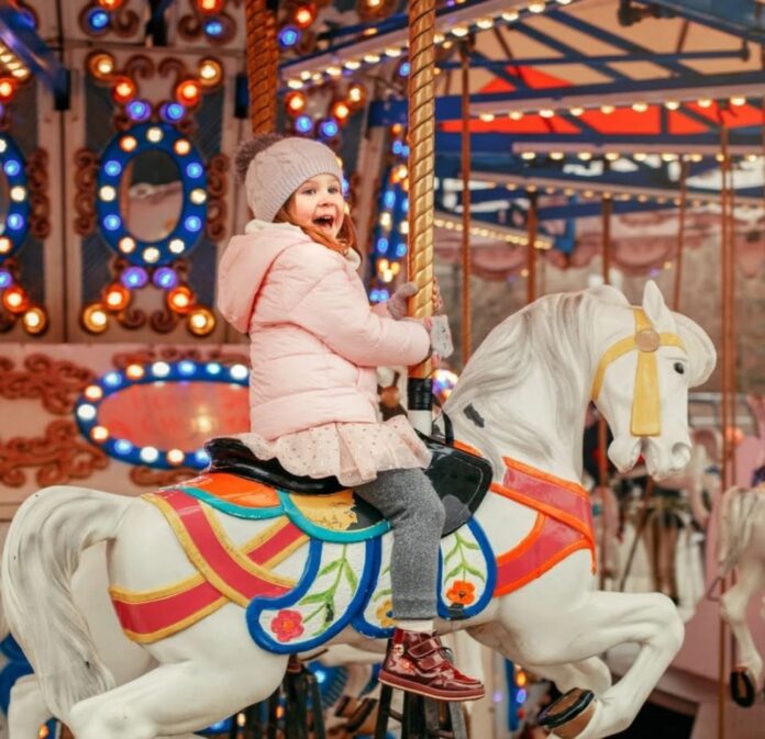653709214_10174306216325694_795365807460953861_n Young girl sitting on a merry go round horse