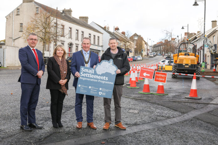 Four people standing on a street with construction works to their left, holding a sign saying Small Settlements.
